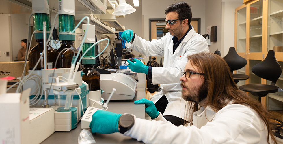 Two male students wearing white lab coats working in a lab.